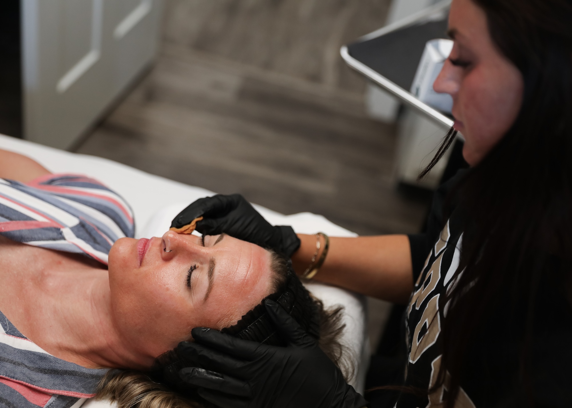 A female patient lies on a treatment table with her eyes closed. A Spry provider gently applies a deep exfoliation technique, using a special applicator pad, as part of the patient's hyperpigmentation treatment in Waterloo.